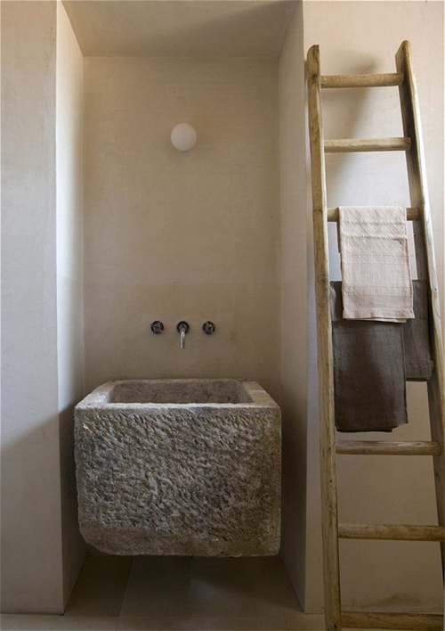 minimalistyczna łazienka rustykalna z umywalka wykutą z surowego szarego kamienia, z drabiną zastosowana jako podajnik do ręczników