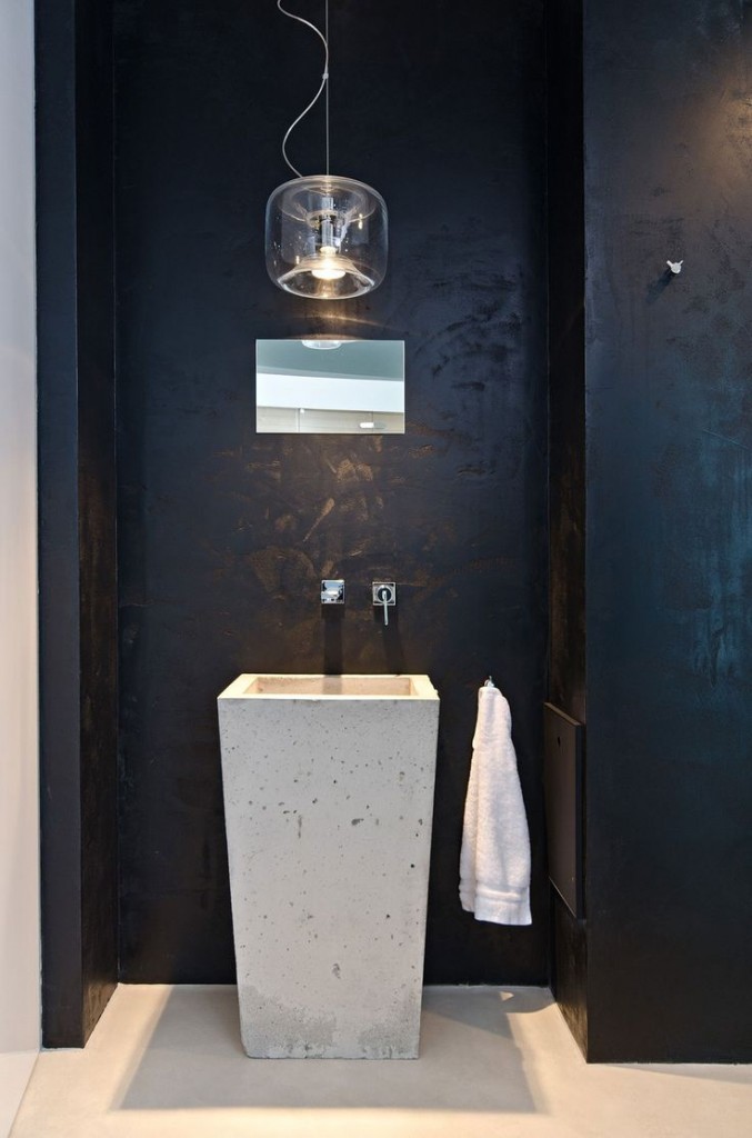 czarna łazienka wyposażona w wysoką surową betonową umywalkę w kształcie kwadratowej donicy i nowoczesną lampę