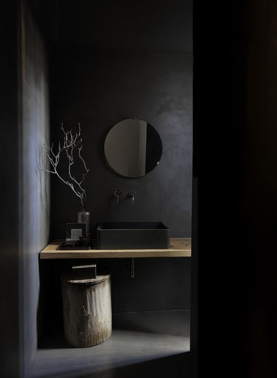 ciemne okrągłe lustro idealnie integruje się z ciemnym wnętrzem łazienki