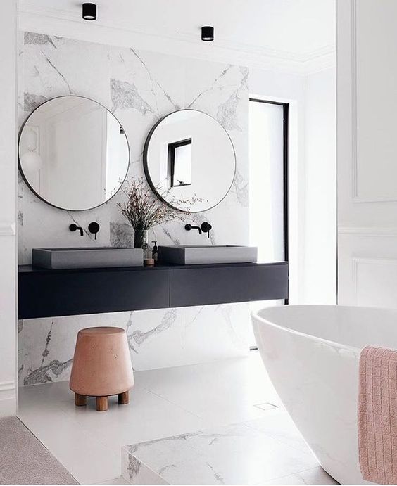 marmurowe ściany i betonowe umywalki, do tego okrągłe lustra w cienkich a głębokich, czarnych ramach, minimalistycznych